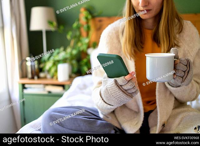 Woman holding tea cup and using mobile phone at home