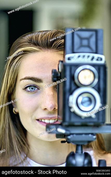 Portrait of a young beautiful caucasian woman in her 20's with blue eyes photographing with an old vintage camera on a tripod outdoor