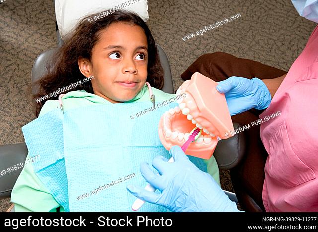Dental nurse showing girl how to clean teeth