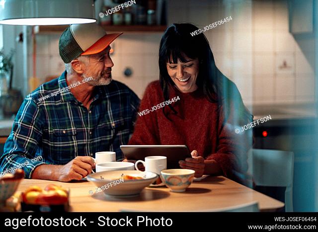 Cheerful couple using tablet PC at table in kitchen