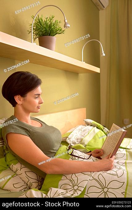 Mid-adult woman reading book in bed, alone in bedroom