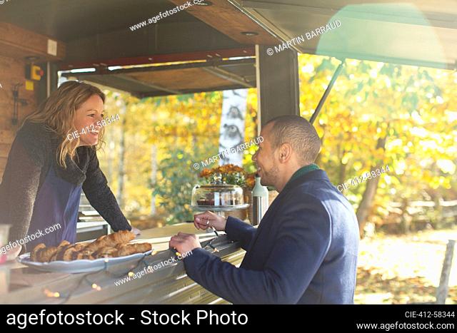 Happy friendly food cart owner talking with customer in autumn park