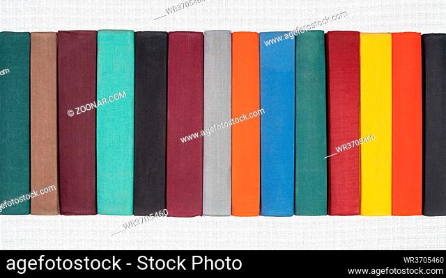 Stack of old hardcover books on white abstract textile background. Close-up view of multicolored vintage hardback books: black, brown, purple, turquoise, gray