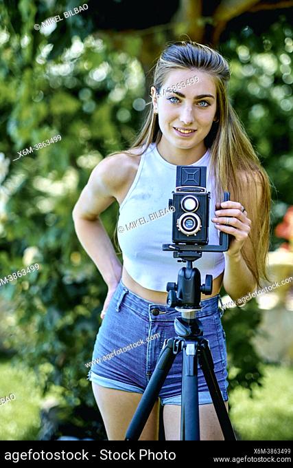Portrait of a young beautiful caucasian woman in her 20's photographing with an old vintage camera on a tripod outdoor in a garden. Lifestyle concept