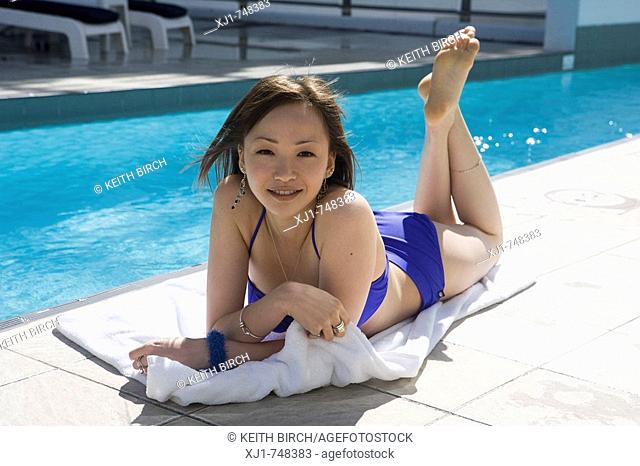 A young Japanese woman lying on a towell beside a hotel complex swimming pool