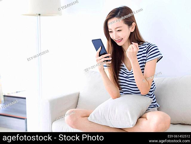 excited young woman looking at her smart phone and smiling while sitting on the sofa at home