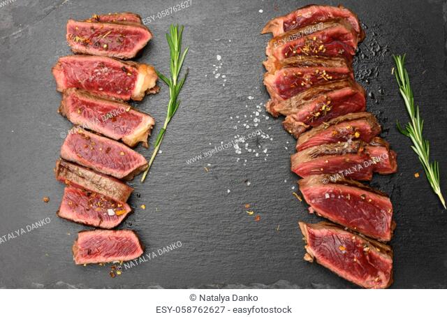 two fried beef steaks cut into pieces on a black board, the degree of doneness rare with blood, top view