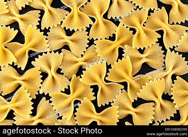 Dry farfalle pasta pattern on black background, top view, flat lay texture