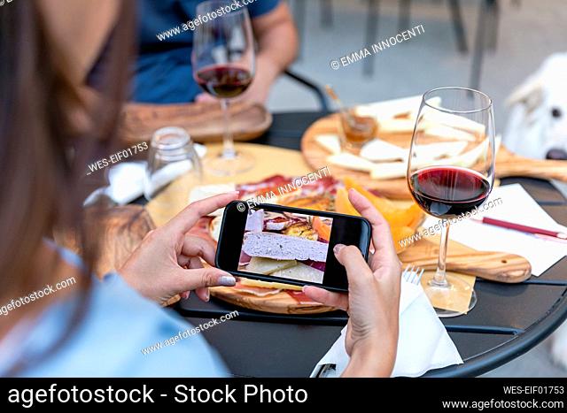 Woman photographing food through smart phone with man at sidewalk cafe