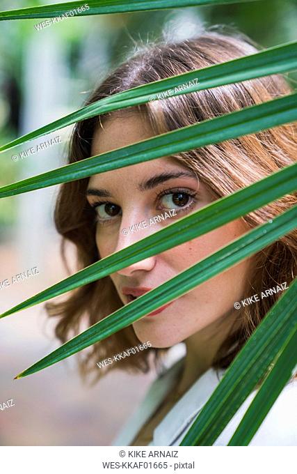 Young woman looking through palm leaf, portrait