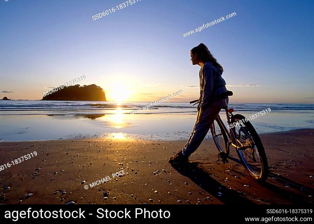 Young woman leaning on bicycle on the beach watching the sun rise