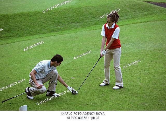 Young Man Teaches a Young Woman How to Play Golf