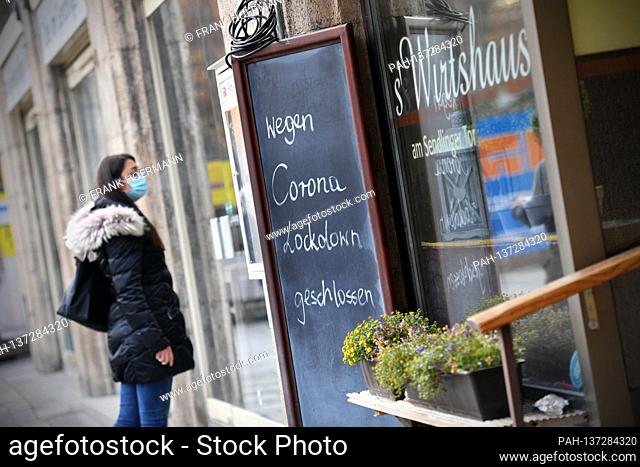 Topic picture: Coronavirus pandemic / consequences for gastronomy. A young woman stands with face mask, mask in front of a locked door of an inn next to a sign:...