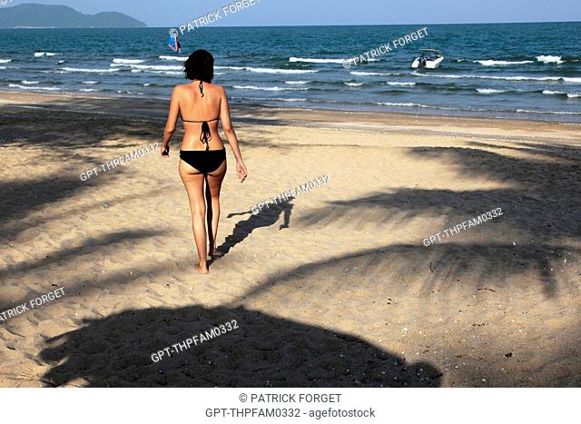 VACATIONING WOMAN WALKING ON THE BEACH AT THE CORAL HOTEL, BANG SAPHAN, PRACHUAP KHIRI KHAN, THAILANDE, ASIA