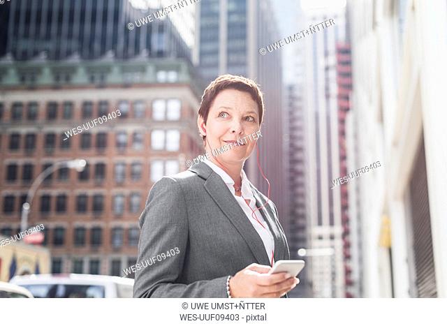 USA, New York City, businesswoman in Manhattan with with cell phone and earphones