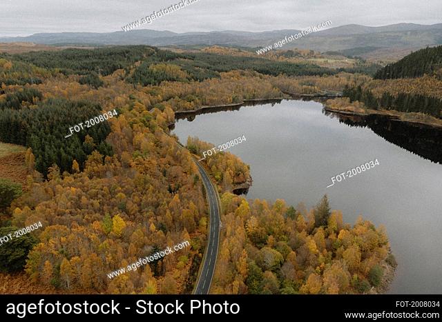 Aerial view road among autumn trees along lake in Scottish Highlands, Scotland