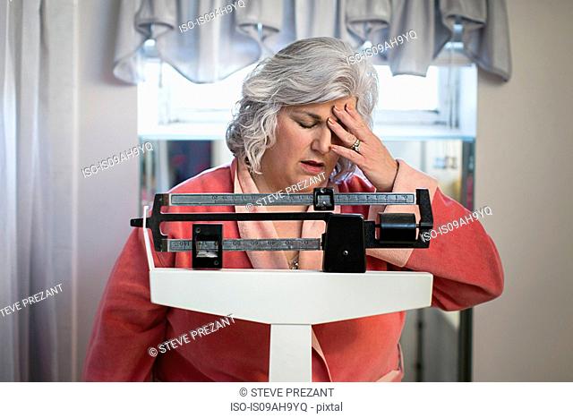 Unhappy mature woman on bathroom weighing scales