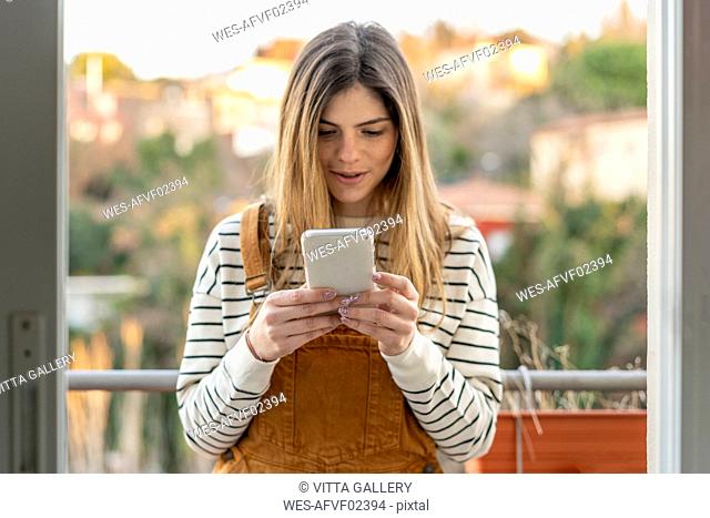 Portrait of young woman standing on balcony looking at cell phone