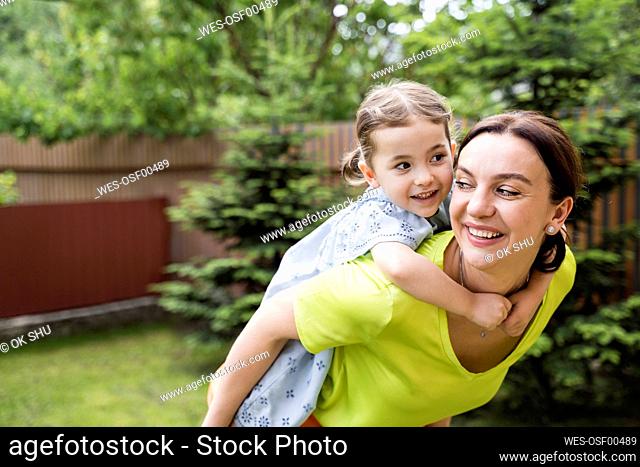 Smiling mother giving backpack ride to daughter at back yard