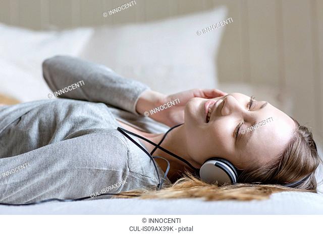 Woman lying on bed wearing head phones, eyes closed smiling