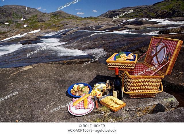 Picnic hamper beside a waterfall with a Helicopter in the background in the Mealy Mountains, Southern Labrador, Newfoundland & Labrador, Canada