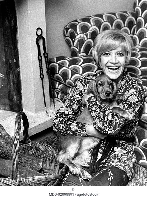 Portrait of Italian painter, director and showgirl Gisella Pagano clasping in her arms a cocker spaniel and smiling. Lierna, 1970s
