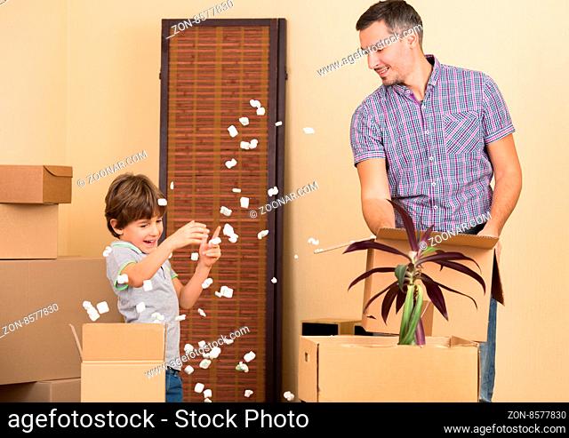 Father and his little son playing in a new house or apartment while unpacking all the things from boxes or cardboards
