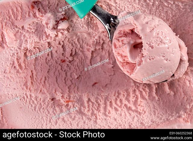 Top view of strawberry flavour ice cream with scoop in box. Focus on scoop with ice cream
