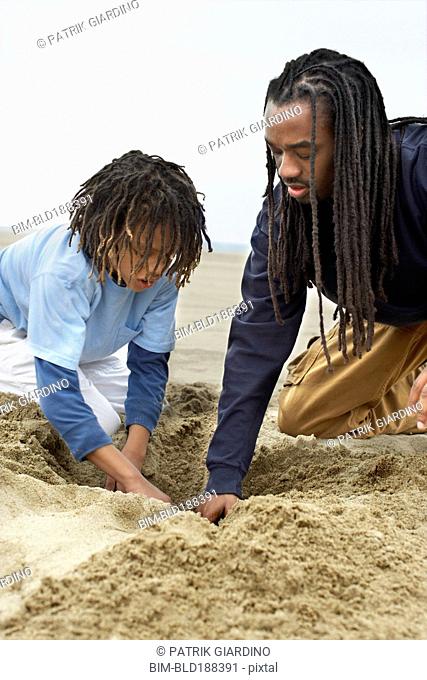 African father and son digging in sand