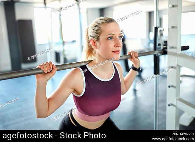 Sportliche junge Frau beim Training der Beinmuskeln in der Langhantelstation