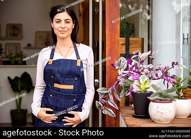 Young adult woman wearing apron standing in plant nursery