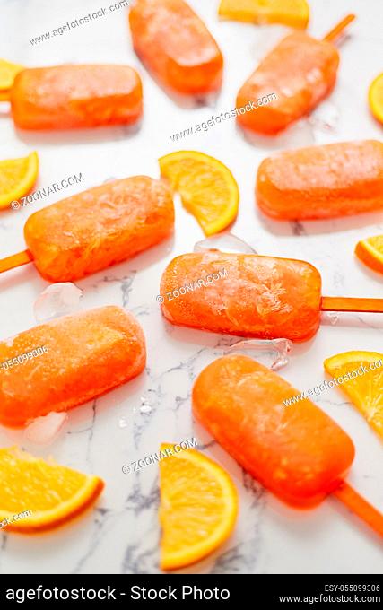 Homemade frozen popsicles made with oragnic fresh oranges placed with ice cubes on marble table. Flat lay, top view