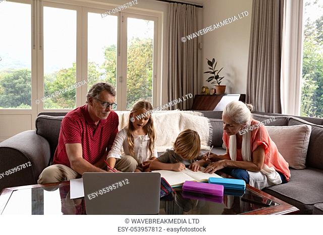 Front view of Caucasian grandparents helping grandchildren with homework in living room at comfortable home