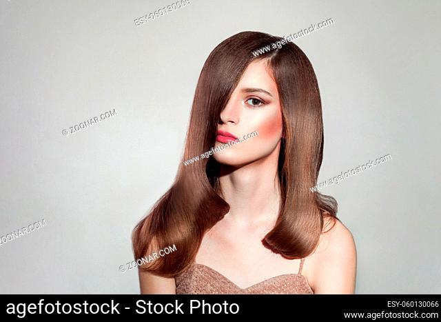 portrait of attractive brunette woman with bright makeup and straight shiny hairs, posing on isolated grey background. indoor, studio shot on copy space