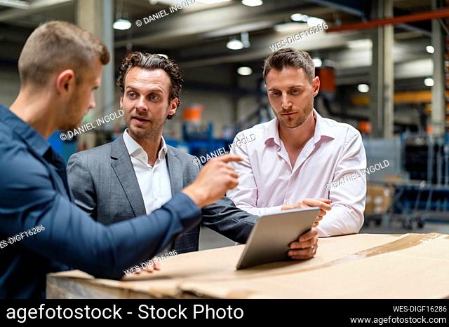 Male colleagues discussing over digital tablet in factory