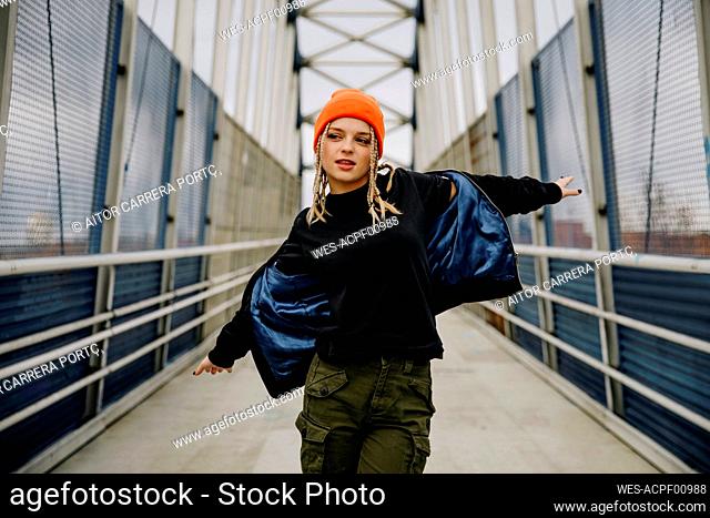 Beautiful woman wearing jacket with arms outstretched dancing on footbridge