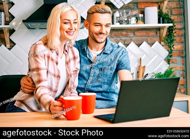 Happy couple drink coffee and using laptop relax together at their kitchen at home