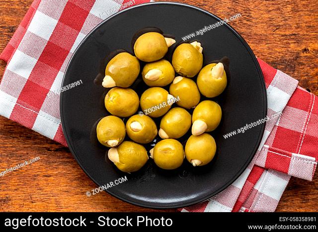 Pitted green olives stuffed with almonds on plate on wooden table. Top view
