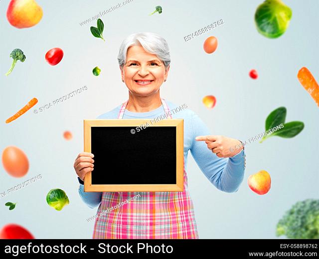 smiling senior woman in apron with chalkboard