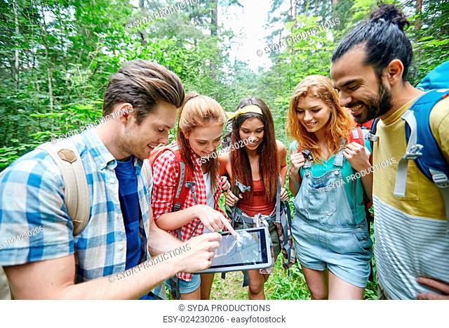 technology, travel, tourism, hike and people concept - group of smiling friends walking with backpacks and map on tablet pc computer screen looking for location...