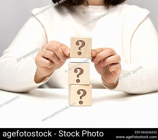 female hand holding a wooden cube with a question mark, concept of answers and questions, suspense and solution methods, close up