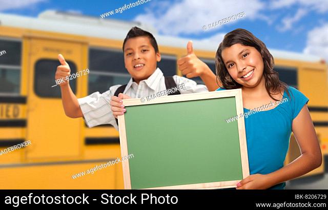 Young hispanic students with blank chalkboard near school bus