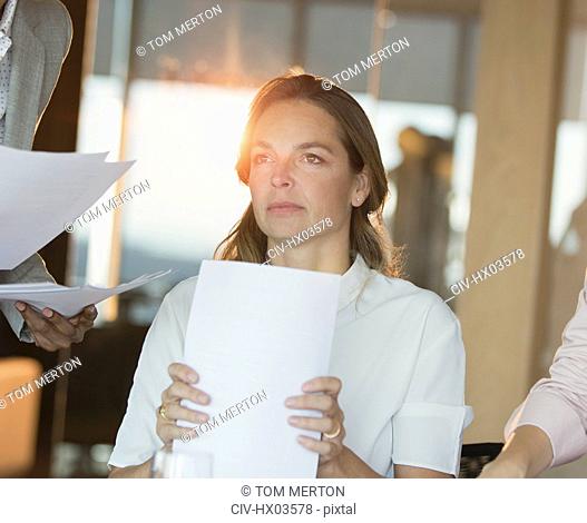 Serious, pensive businesswoman with paperwork looking away in office