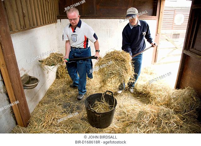 Two men with learning disabilities helping to muck out a stable on a trip to an animal centre