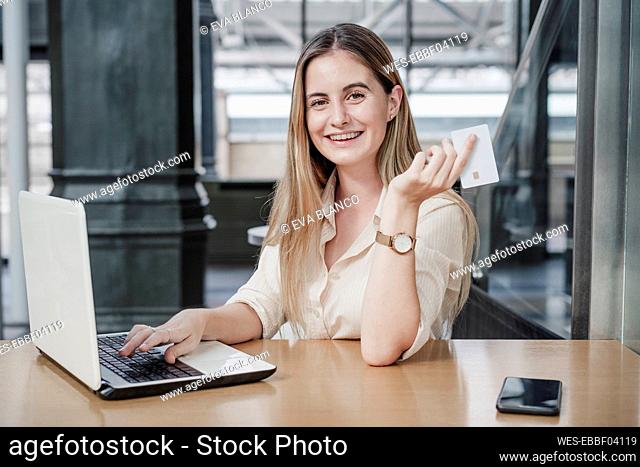 Happy female freelancer sitting with laptop and credit card at cafe