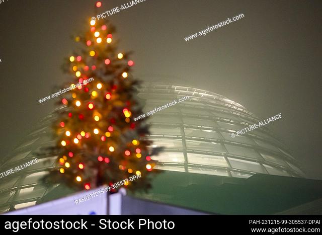 15 December 2023, Berlin: A Christmas tree lights up in the morning fog in front of the dome of the Reichstag building. On the Bundestag's agenda today is the...
