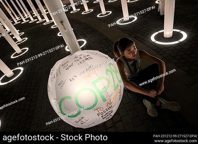 12 December 2023, United Arab Emirates, Dubai: A woman sits next to a globe labeled ""COP28"". The World Climate Conference has gone into extra time after a...