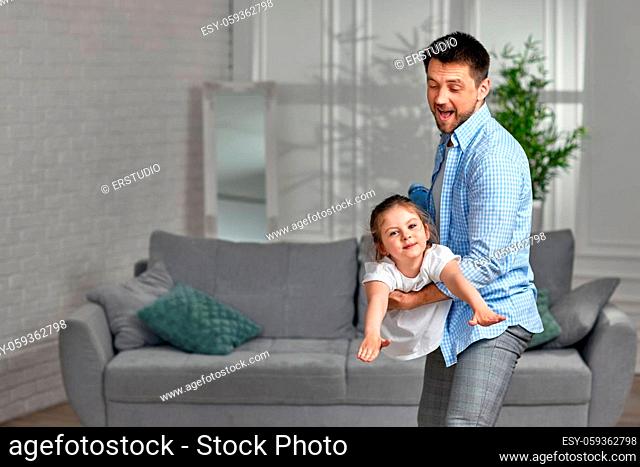 Happy little child girl flying in fathers arms looking at camera at home