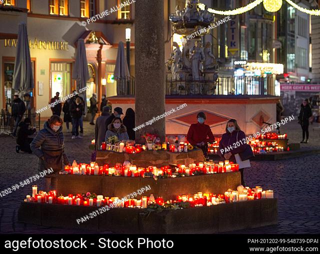 02 December 2020, Rhineland-Palatinate, Trier: People place in the evening at the market cross (v) and the Petrusbrunnen for the victims of a rampage candle The...