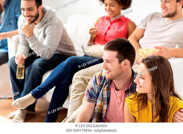 friendship, people and entertainment concept - happy friends with popcorn and beer watching tv at home